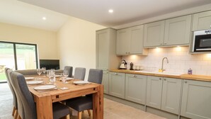 A modern kitchen with a wooden dining table set for six, light-colored cabinets, and a built-in microwave. - Bears Court Barn 3 (Cheltenham)