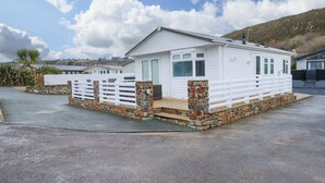 A white mobile home with stone pillars, a white fence, and a paved driveway. - Un Diwrnod The Warren T22 (Pwllheli)