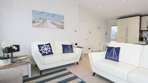 A modern living room with two white sofas, a striped rug, and nautical-themed pillows. - Un Diwrnod The Warren T22 (Pwllheli)