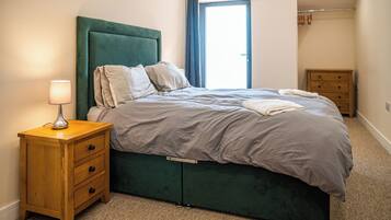 A neatly made bed with a green headboard, a wooden nightstand with drawers, and a lamp.