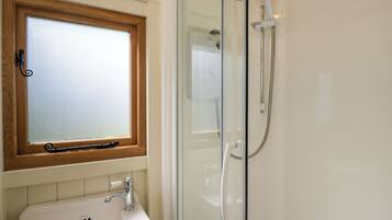 A bathroom with a glass shower enclosure, a white sink, and a frosted window above the sink.