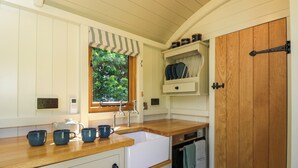 A compact kitchen with a wooden countertop, white cabinetry, a window with a view of greenery, a built-in oven, and a wooden door. - Hazel (Witney)