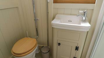 Un baño con inodoro blanco, asiento de madera, lavabo blanco y un pequeño cubo de basura.