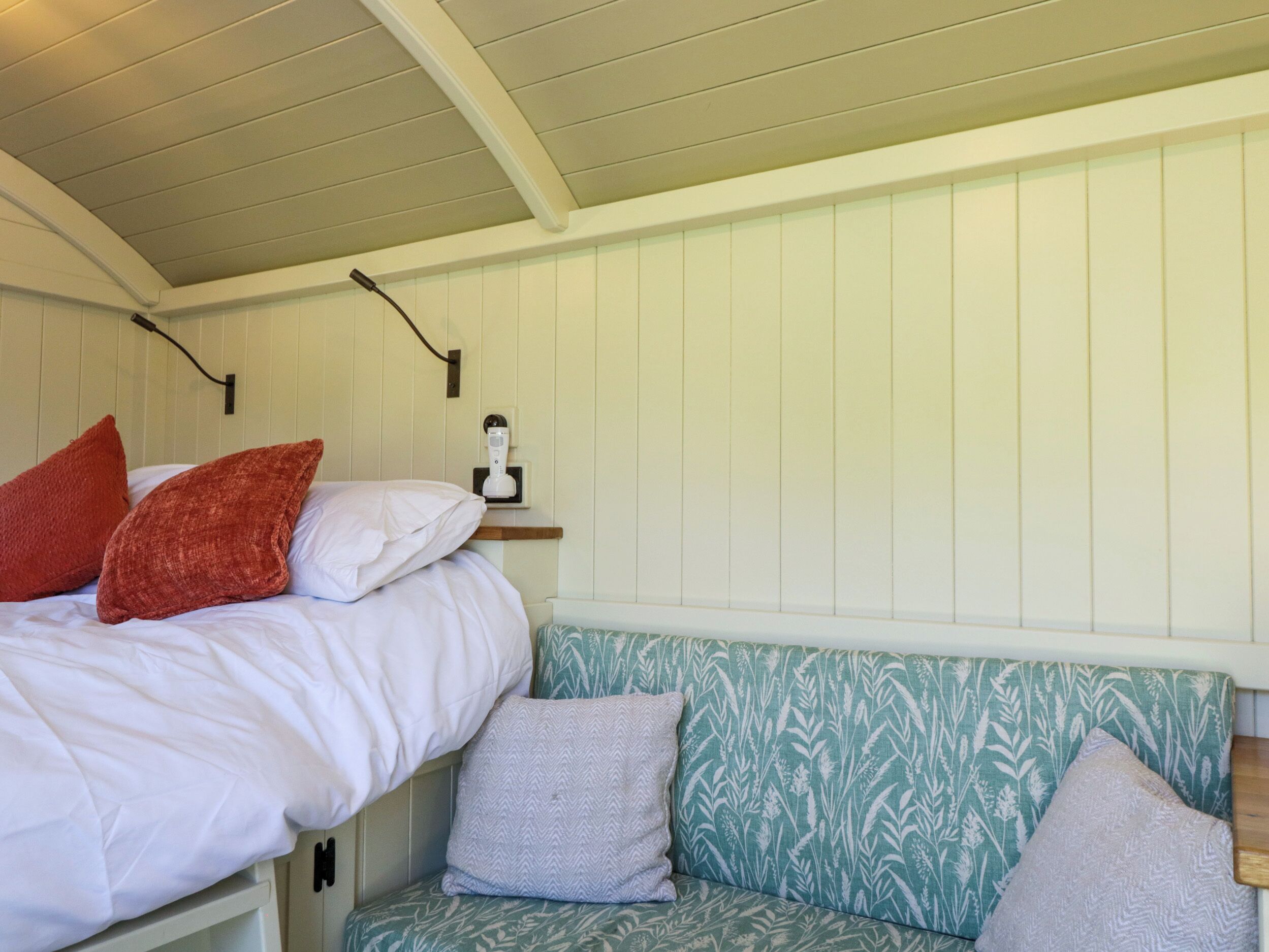 A bedroom with a bed, a bedside table, a wall-mounted lamp, and a patterned bench.
