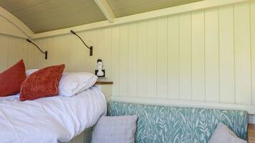 A bedroom with a bed, a bedside table, a wall-mounted lamp, and a patterned bench.