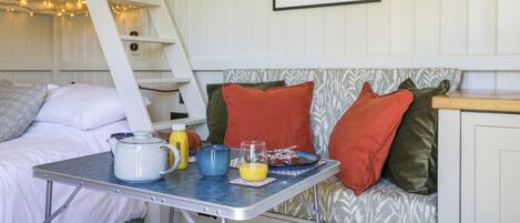 A cozy room with a bunk bed, a dining table with breakfast items, a cushioned bench, and a framed floral artwork on the wall.