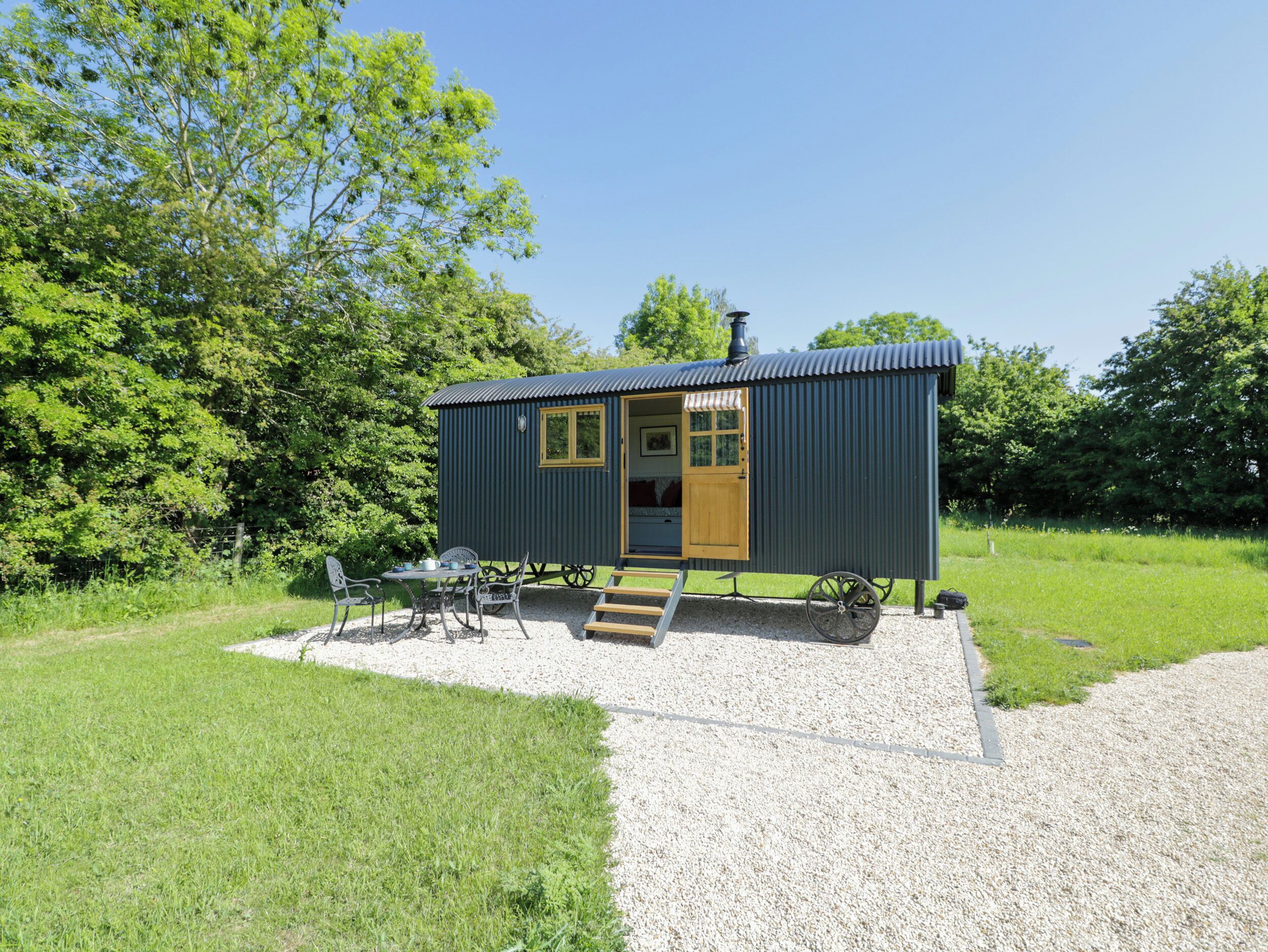 A small, single-story cabin with a gravel driveway and a wooden deck.