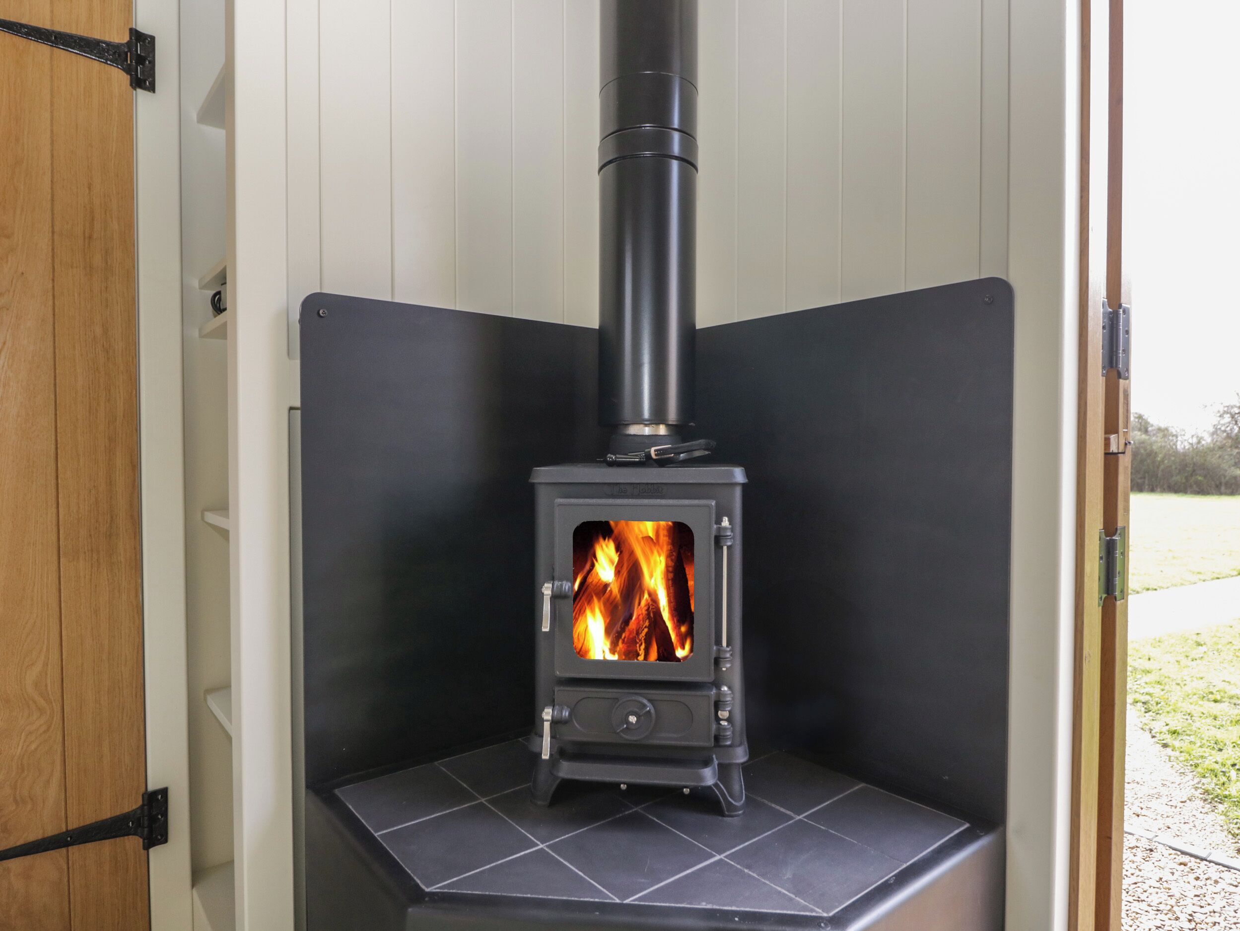 A wood-burning stove in a corner of a room with white walls and a black tiled floor.