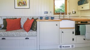 A cozy kitchenette with a wooden countertop, a sink, and a stove. There is a window with a view of greenery outside.