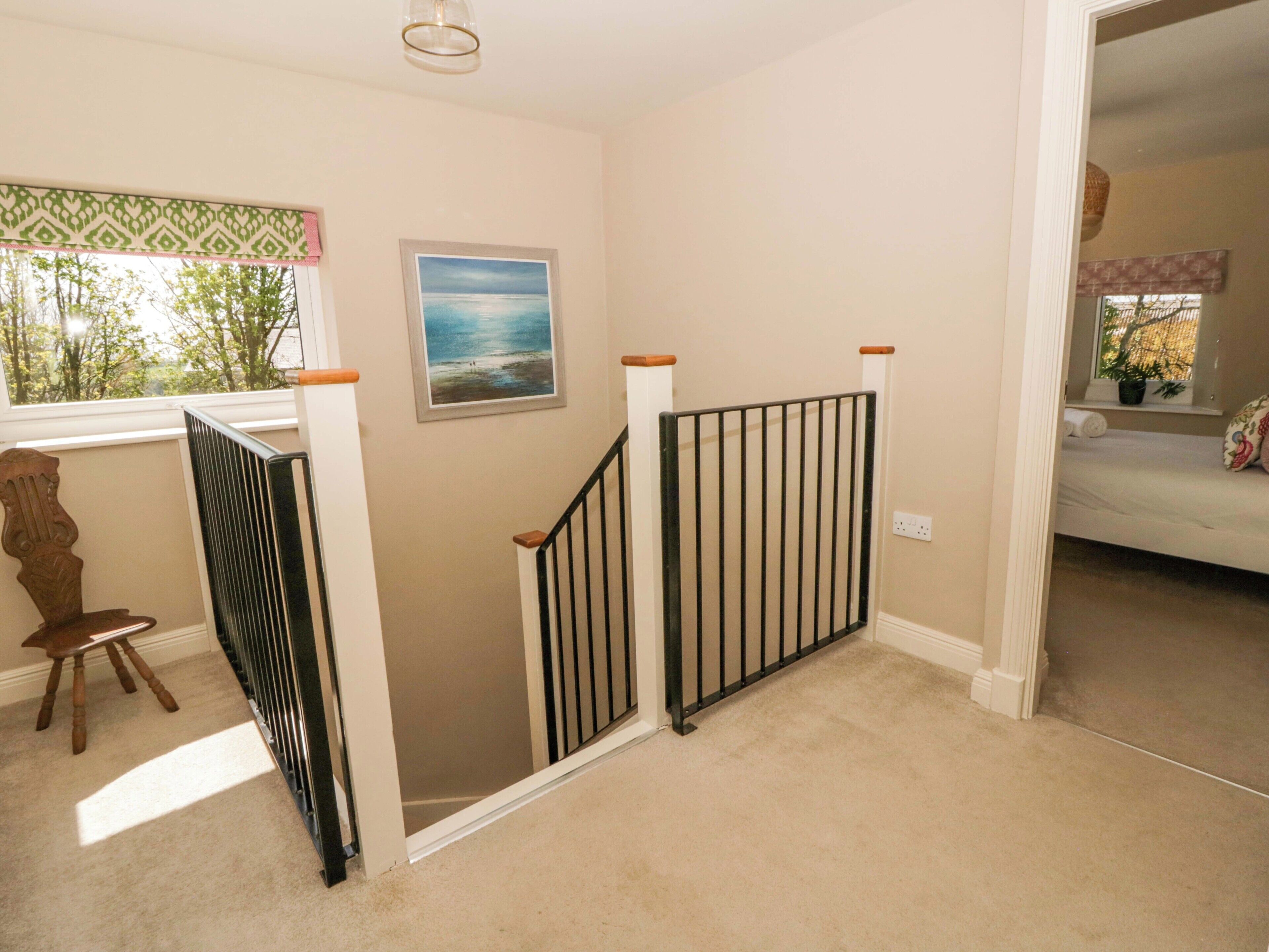 A staircase with a black metal railing, a wooden chair, a framed picture, and a bed in the adjacent room.