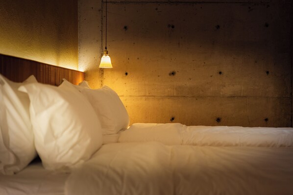 Een bed met witte beddengoed en een hangende lamp in een kamer met een houten hoofdbord en een gestructureerde wand.