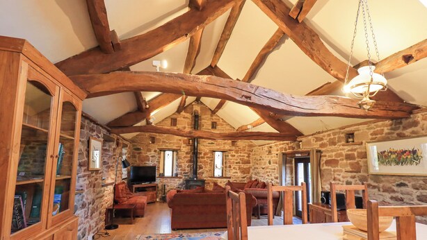 Ein rustikaler Raum mit freiliegenden Holzbalken, Steinwänden, Kamin, Fernseher, Sofa und Esstisch.