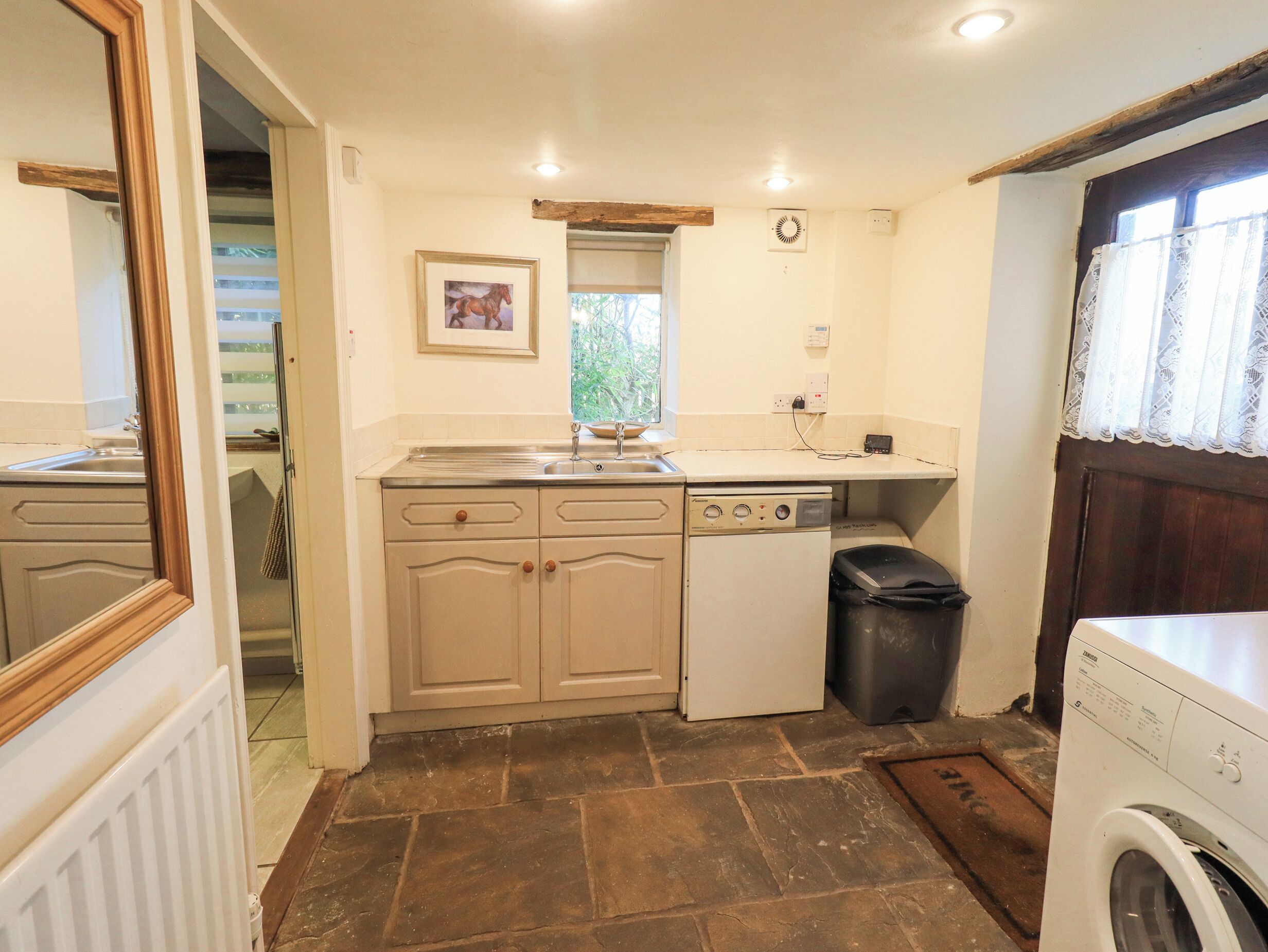 A compact kitchen with a built-in dishwasher, a sink, and a window with a view of greenery.