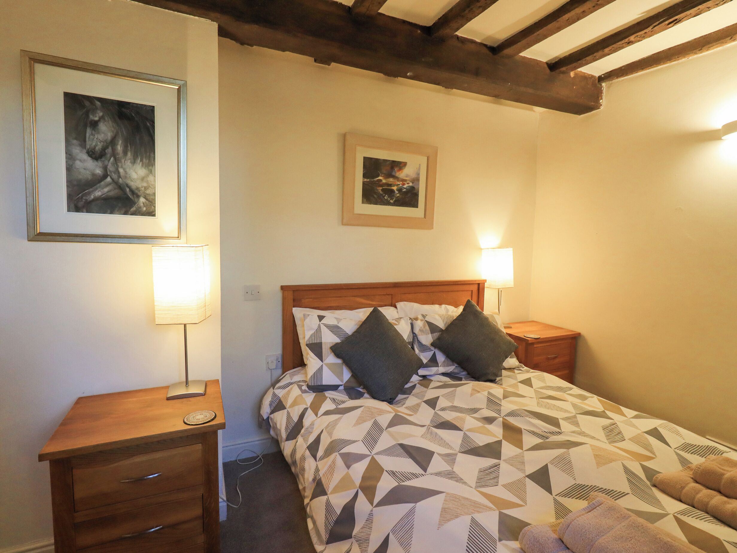 A bedroom with a wooden bed, two bedside tables, a nightstand, and two wall-mounted lamps.