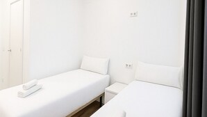 A hotel room with two single beds, a wooden floor, white walls, and a door. - Hostal Bernabeu (Madrid)
