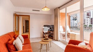 Un salon moderne avec des canapés orange, une petite table en bois et un téléviseur. Il y a un balcon avec vue sur les immebles.