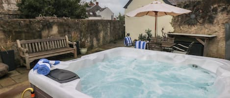 A hot tub in a backyard with a bench, a table, and a chair.
