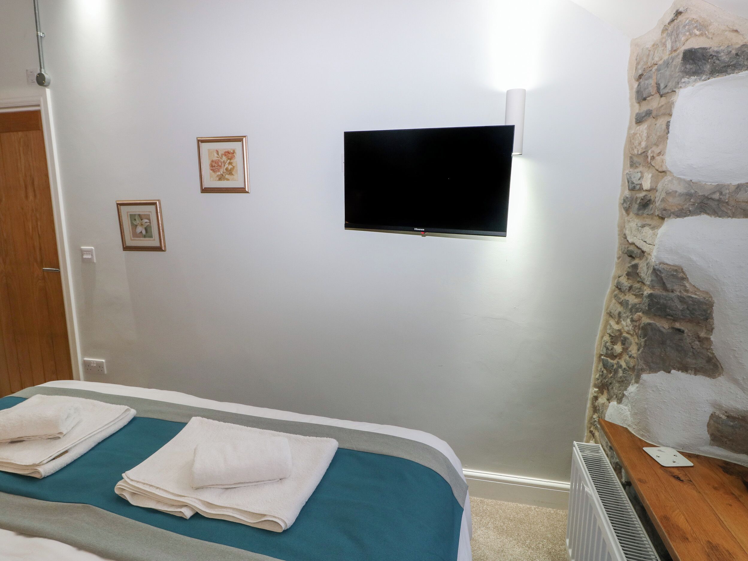 Un dormitorio con cama, un televisor de pantalla plana montado en la pared y una pared de piedra.