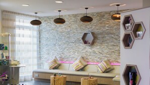A modern spa room with a stone wall, a beige sofa with striped cushions, two wooden side tables, and pendant lighting. - Una, Lodge 77 (St Ives)