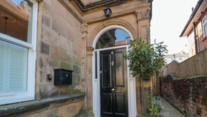 A stone building with a black door, a mailbox, and a narrow alleyway. - Coronation House (Scarborough)