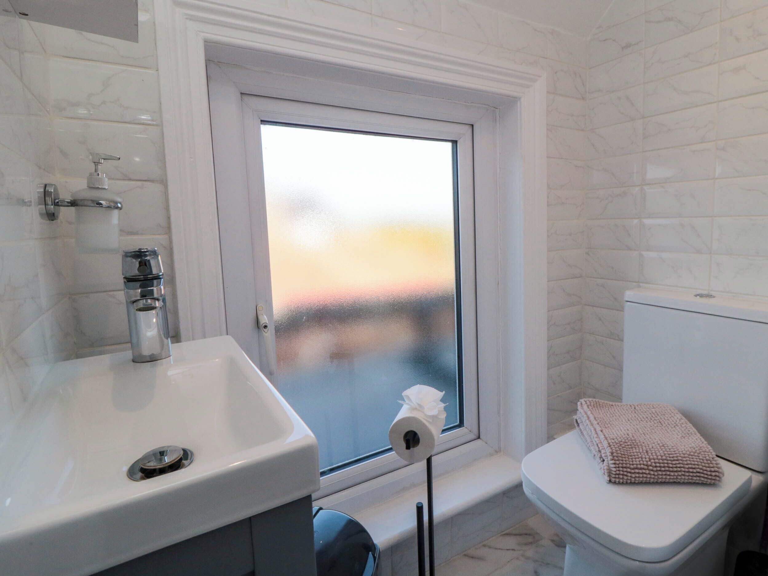 Ein Badezimmer mit Waschbecken, Toilette und einem Fenster mit Milchglas.