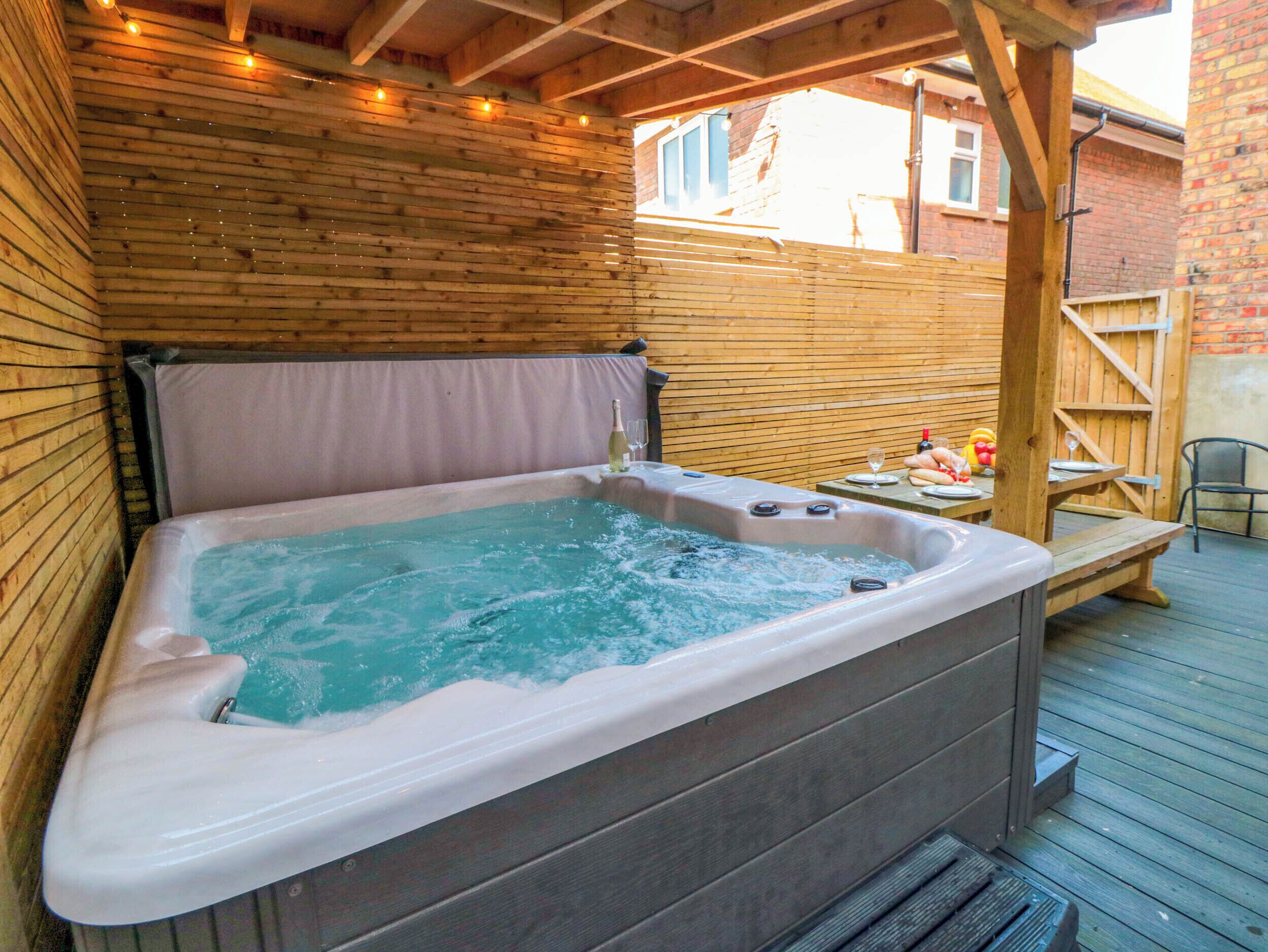 A hot tub with a wooden deck and a brick wall in the background.