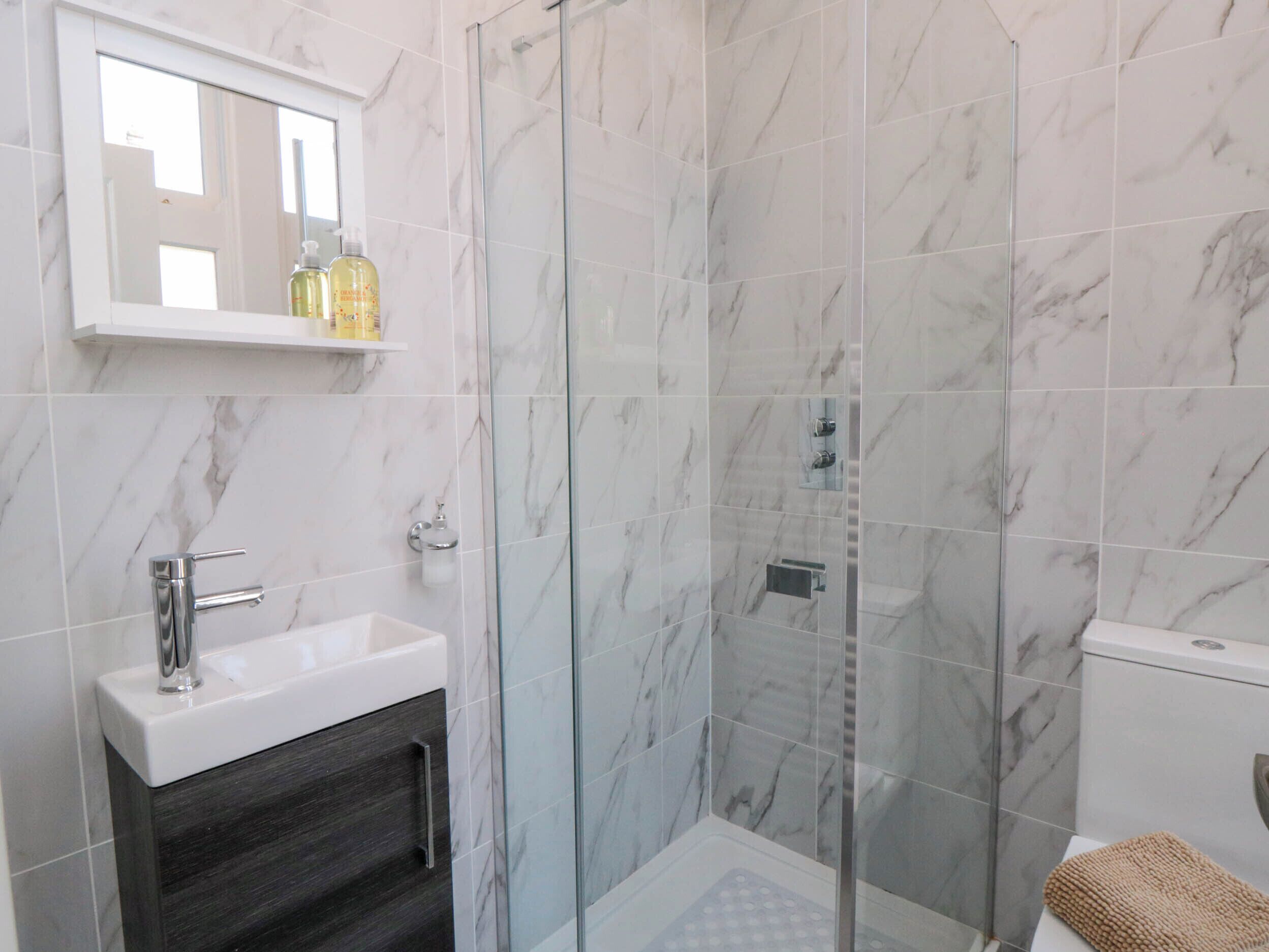 A modern bathroom with a glass-enclosed shower, a white sink, and a dark wood cabinet.