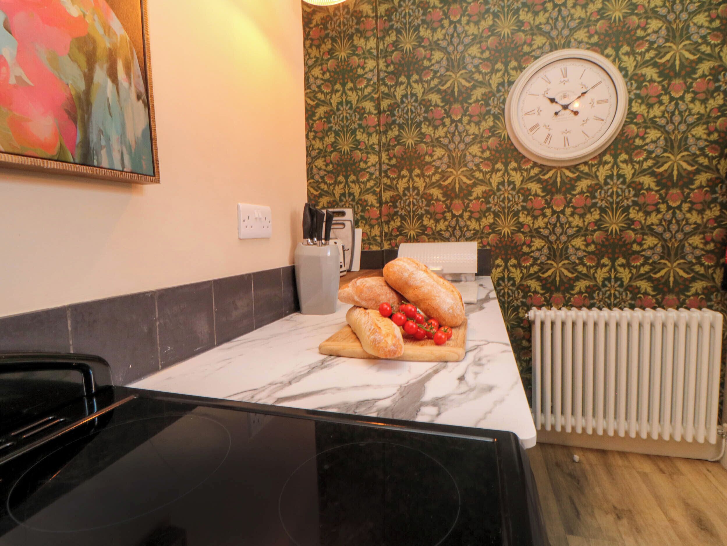 A kitchen with a marble countertop, a clock on the wall, and a radiator.