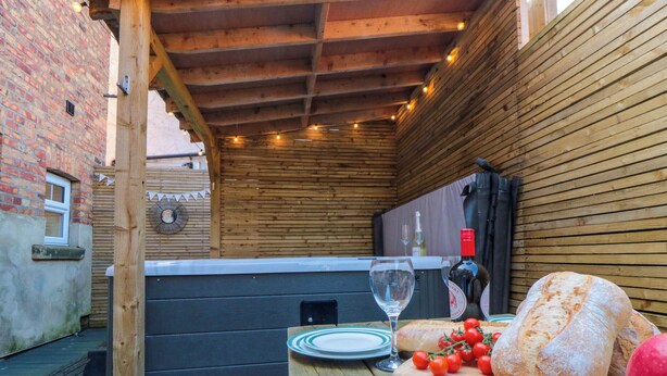 A wooden outdoor seating area with a hot tub, a table with bread and tomatoes, and a wine glass. - Coronation House (Scarborough)