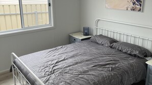 A bedroom with a bed, a nightstand, a ceiling fan, a window, and a beach painting on the wall. - Clearwaters - Single story, 4-bedroom holiday home (Marion Bay)