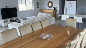A modern living room with a large flat-screen TV, a sofa, and a dining area with a wooden table and chairs. - Clearwaters - Single story, 4-bedroom holiday home (Marion Bay)