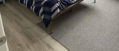 Un dormitorio con una cama, una mesita de noche, una lámpara, un ventilador de techo, una ventana y un cuadro en la pared.
