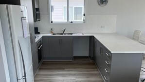 A modern kitchen with grey cabinets, a white refrigerator, and a window above the sink. - Clearwaters - Single story, 4-bedroom holiday home (Marion Bay)