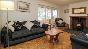 A living room with a sofa, armchairs, a wooden coffee table, a fireplace, and a large window. - 14 Birchwood Road (Lydney)
