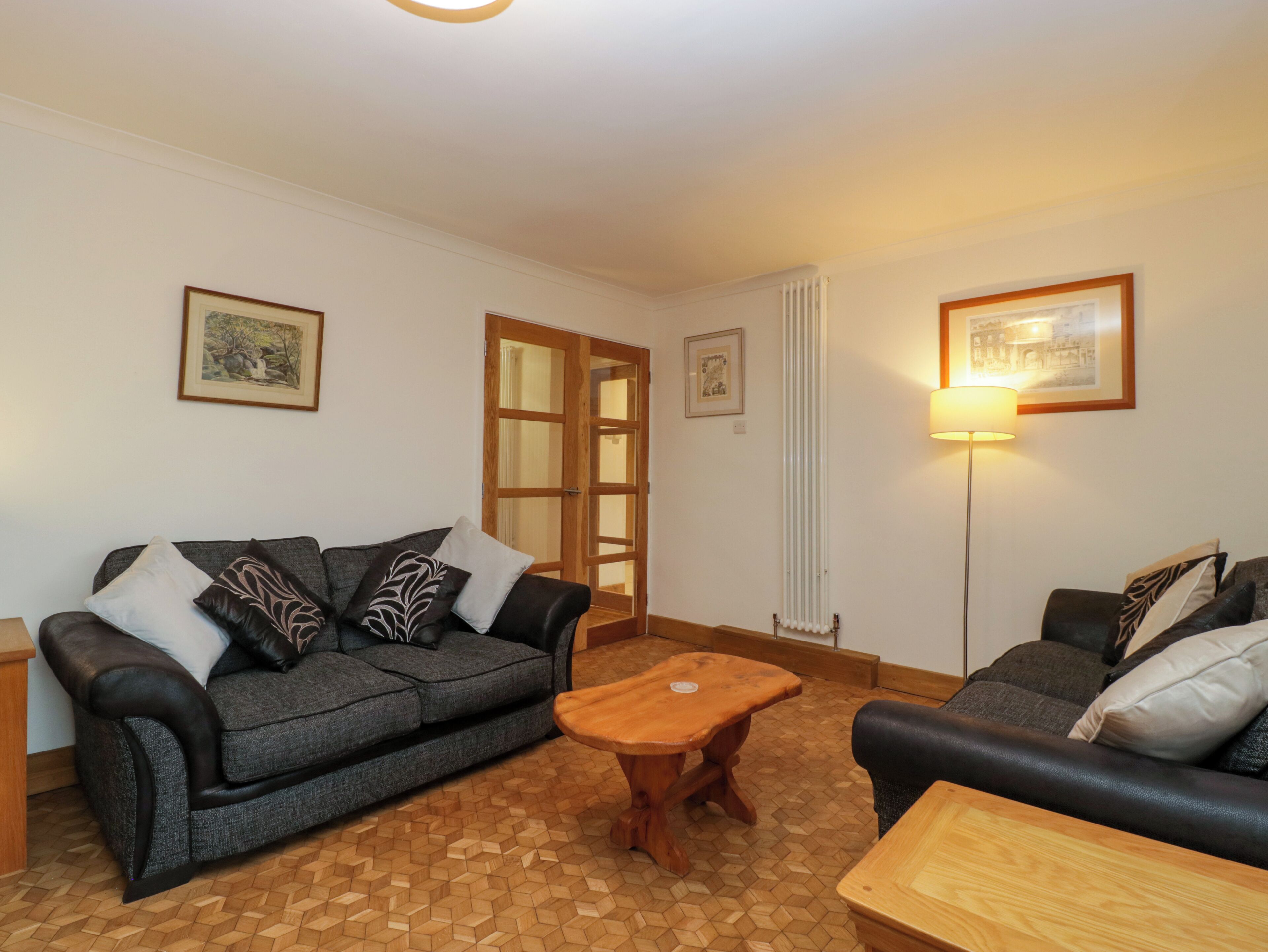 Ein Wohnzimmer mit grauem Sofa, einem Holztisch und einer Lampe. An der Wand hängen zwei gerahmte Bilder.