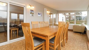 A dining area with a wooden table and chairs, large windows, and a view of the outdoors. - 14 Birchwood Road (Lydney)