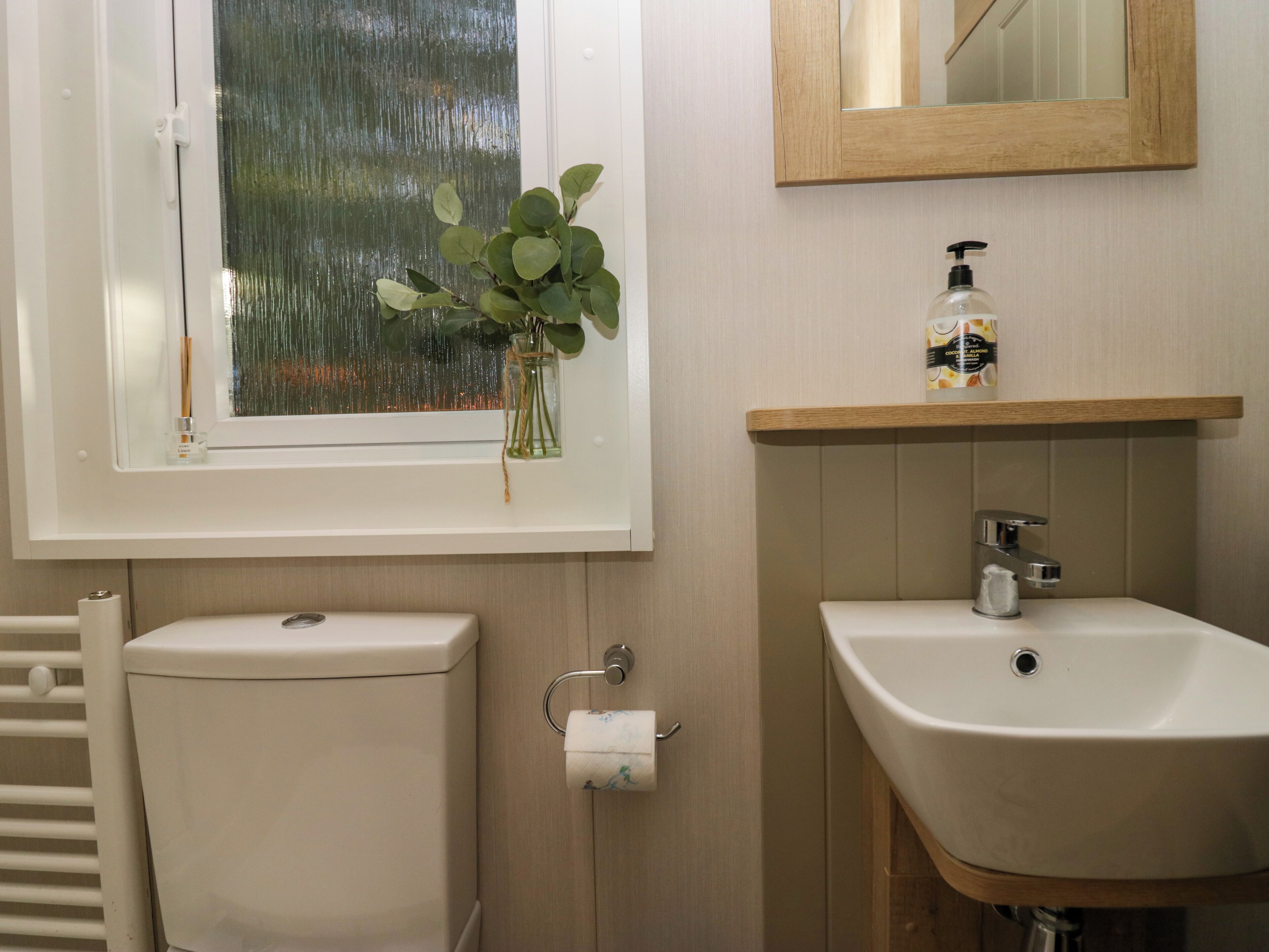 Ein Badezimmer mit Toilette, Waschbecken, Spiegel und einem Fenster mit Pflanze.