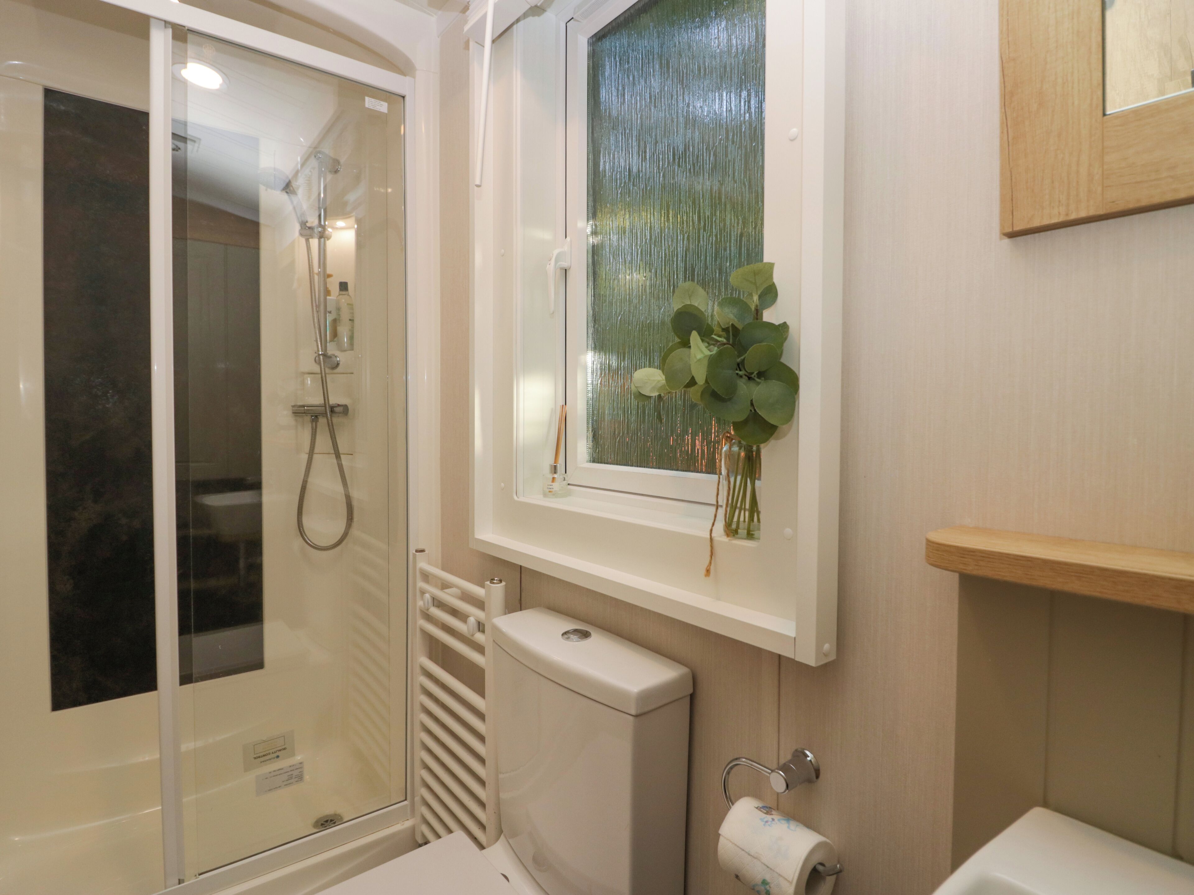 A bathroom with a glass shower enclosure, a toilet, a sink, and a window with a plant.