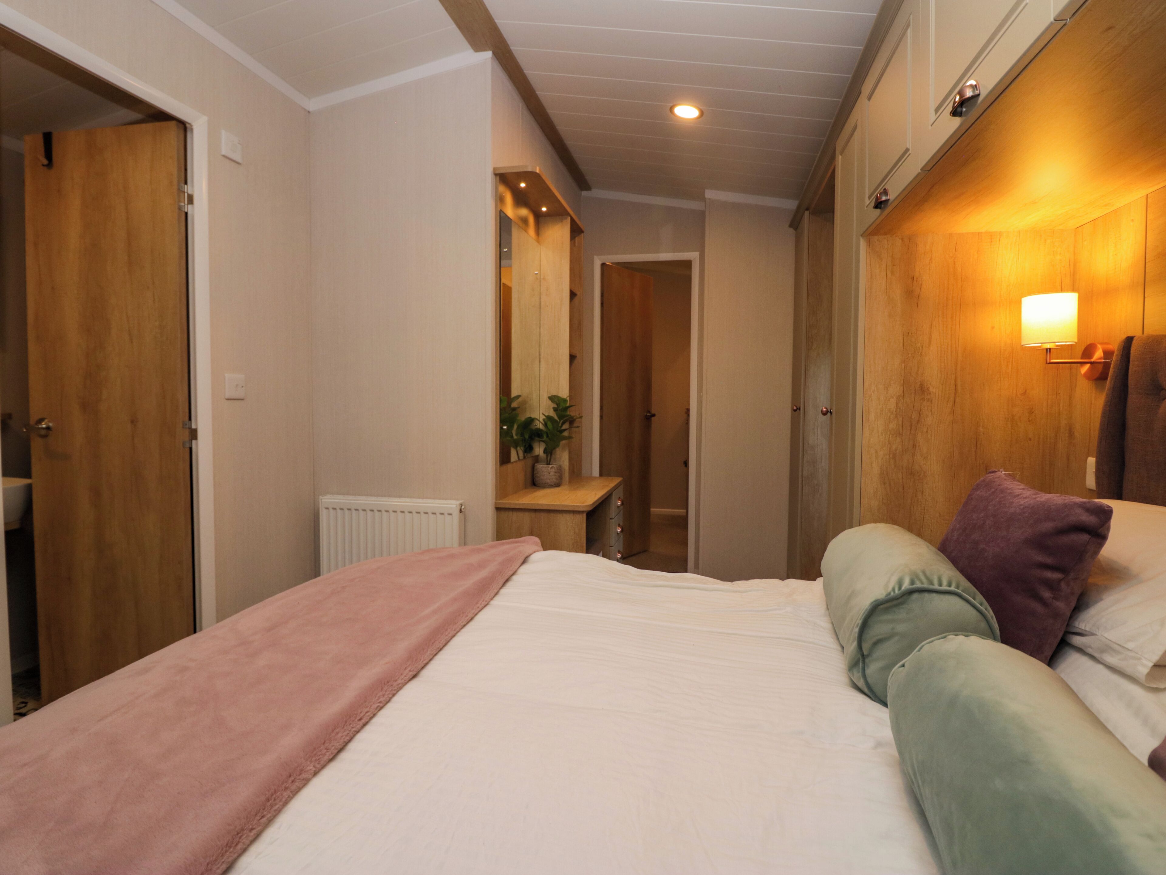 A bedroom with a bed, a bedside table, a nightstand, a mirror, a radiator, and a wall-mounted lamp.