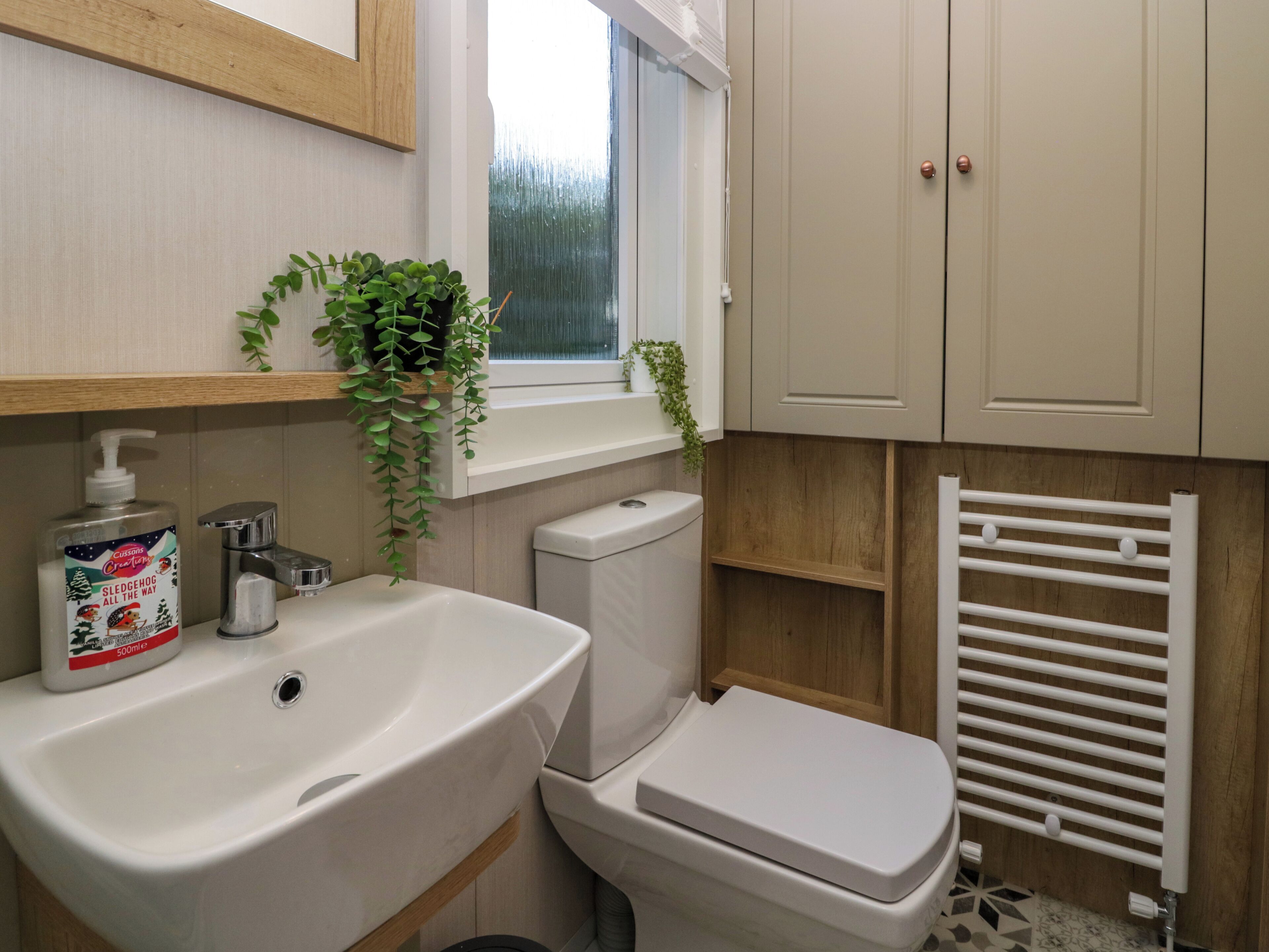 A bathroom with a white sink, toilet, and radiator. There is a window above the sink and a plant hanging on the wall.