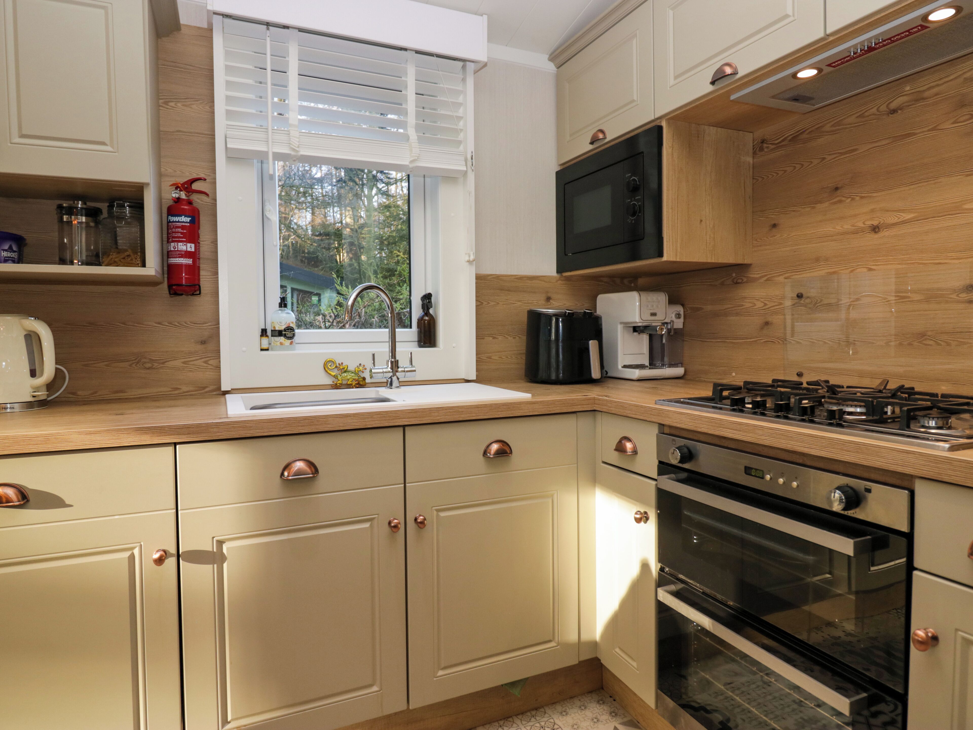 Eine moderne Küche mit Holzausbau, einer Edelstahl-Spüle, einer Kaffeemaschine, einer Mikrowelle und einem Gasherd.