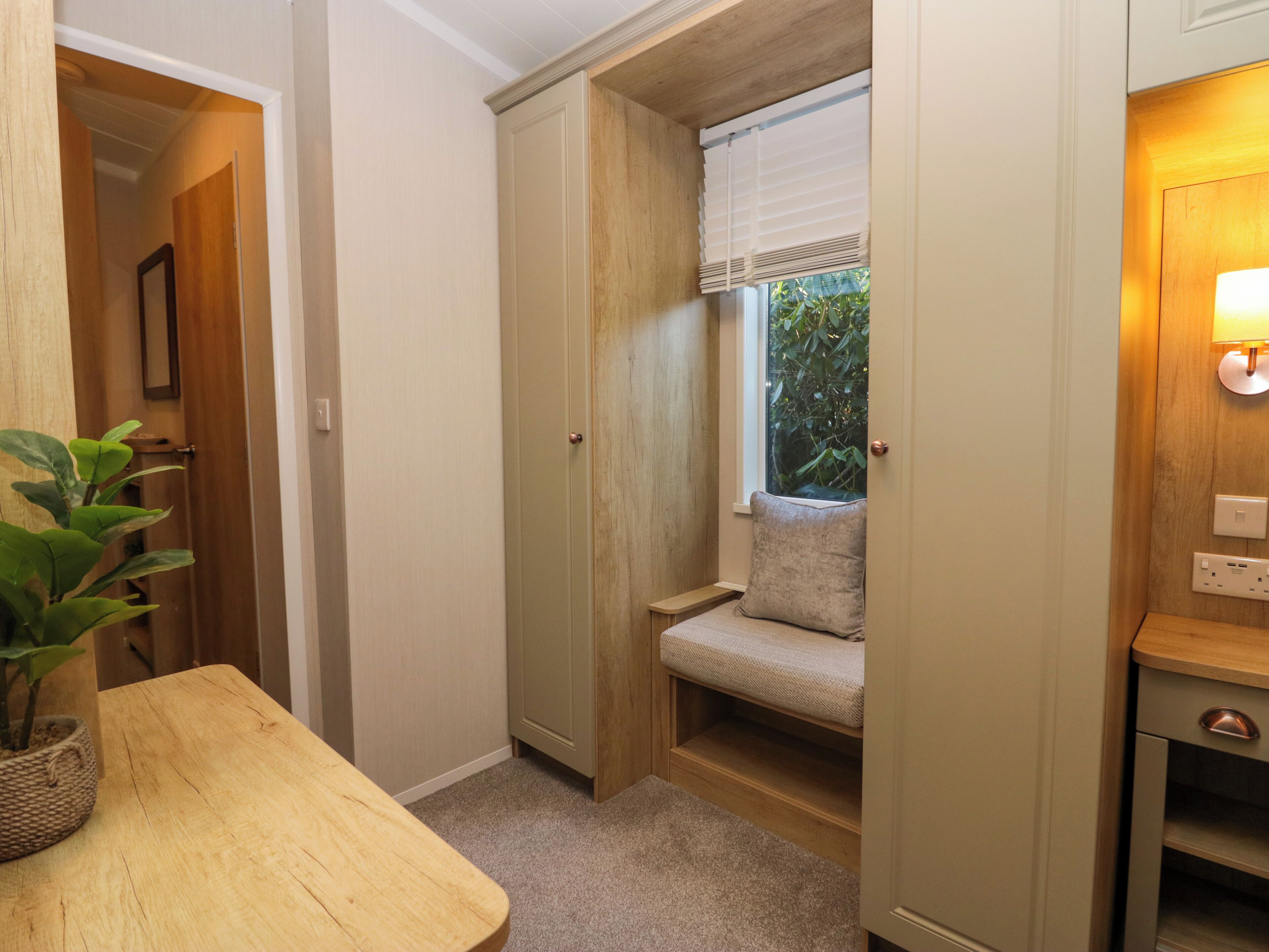 A compact room with a built-in bench, a small table with a plant, and a window with a view of greenery.
