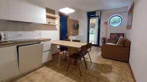 A compact kitchen with a dining table and chairs, a kitchenette, a sofa, and a small window.