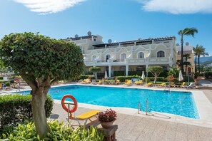 Ein Poolbereich mit Liegestühlen und einem großen Gebäude im Hintergrund.
