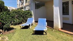 A building with a covered outdoor area, two lounge chairs, and a well-maintained lawn. - Serinamar - Aloha Gardens (Marbella)