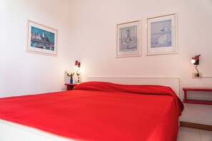 Relax in a serene space with a neatly made bed, a bedside table, and a lamp, surrounded by framed artworks.