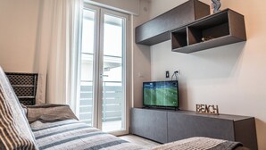 A modern bedroom with a bed, a TV, a sliding door to a balcony, and a shelf with decorative items. - Beachside getaway in Bibione (Bibione)