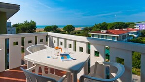 Ein Balkon mit Tisch und Stühlen mit Blick auf Strand und Gebäude.
