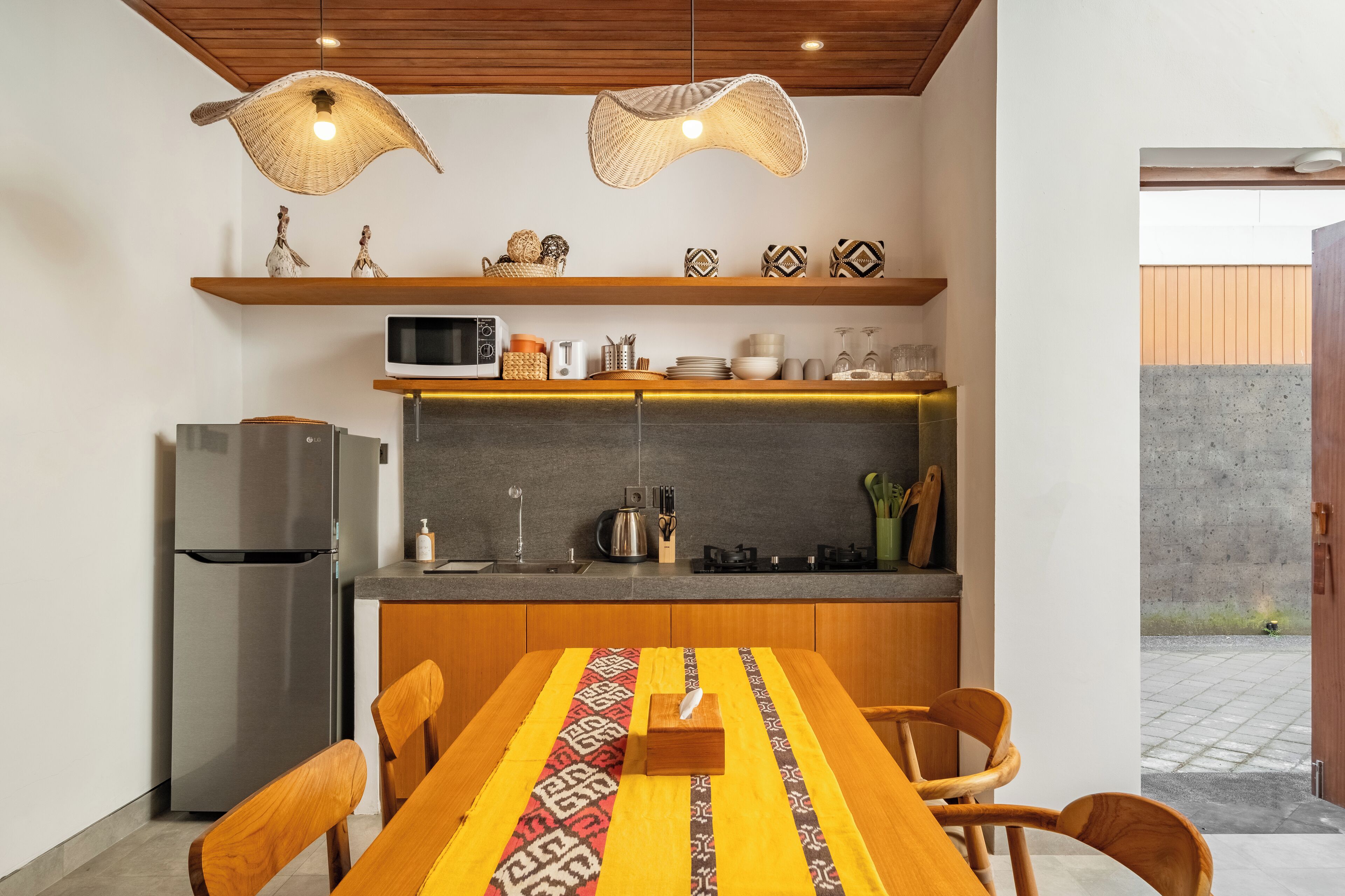 Uma cozinha moderna com micro-ondas embutido, geladeira de aço inoxidável e armários de madeira. Há uma mesa de jantar com cadeiras e um jogo de mesa estampado.
