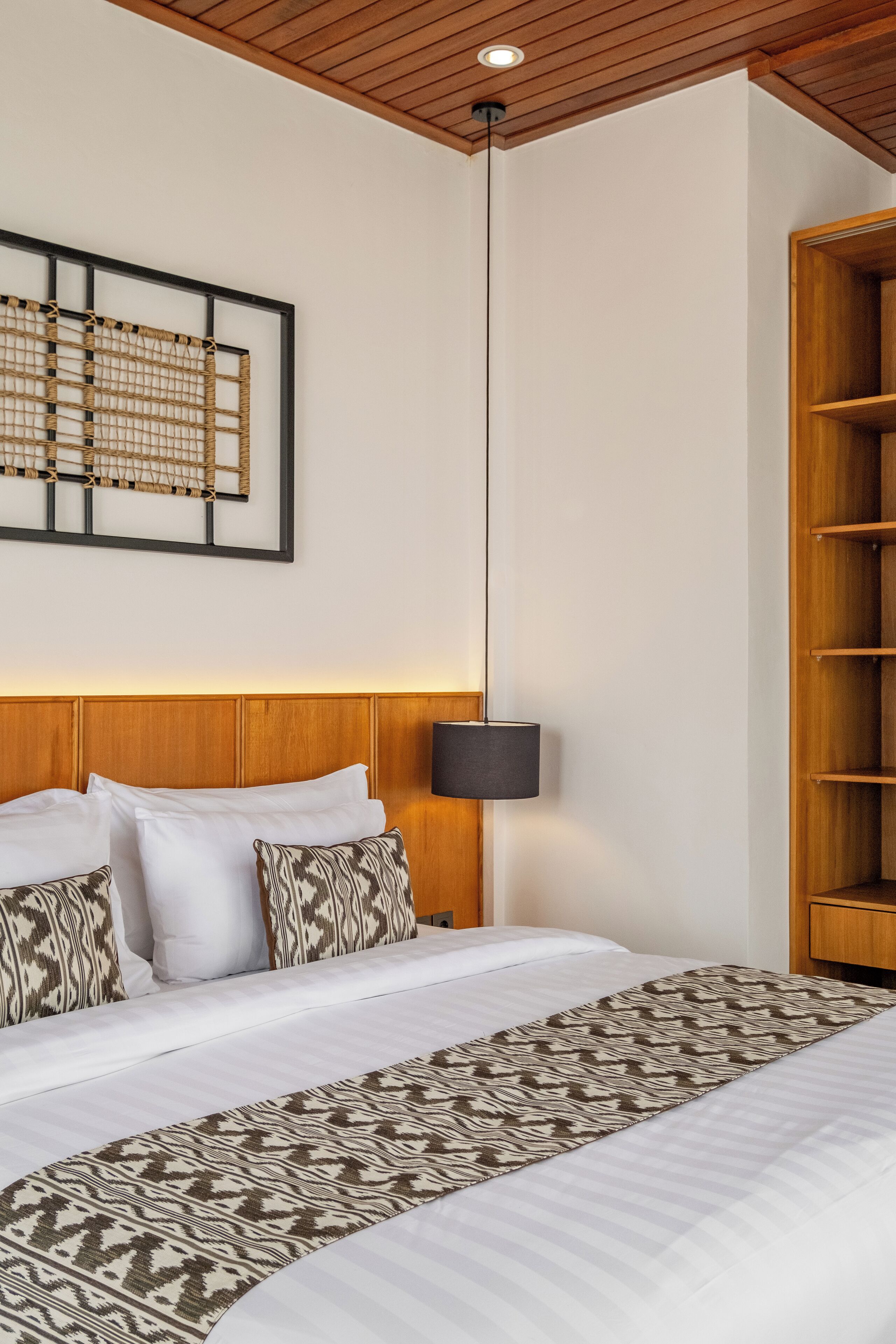 A neatly made bed with patterned pillows, a hanging lamp, and a wooden headboard.